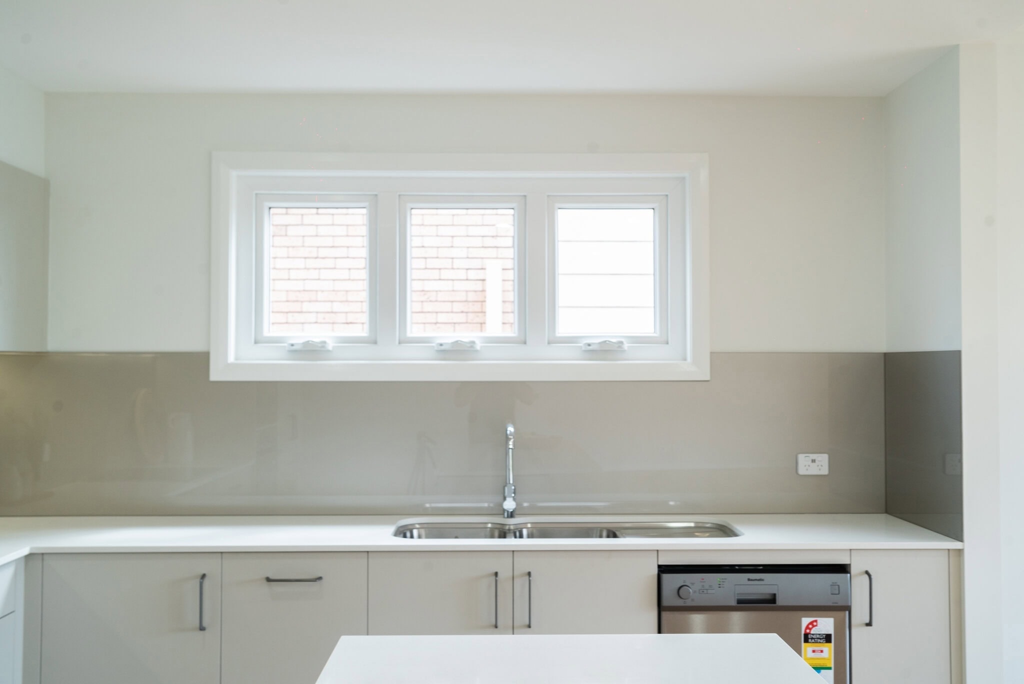 Bright modern kitchen with large window, sleek cabinetry, and built-in dishwasher, ideal for family homes.