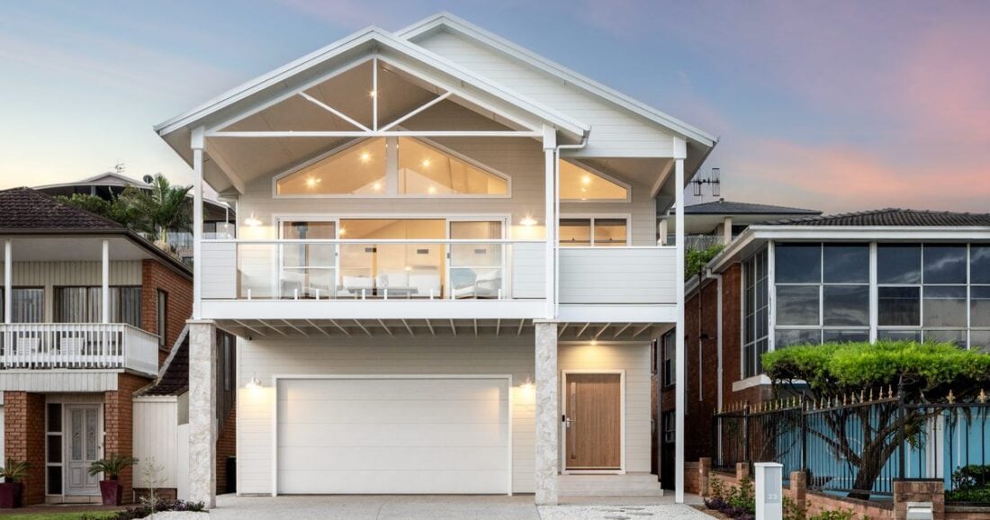 Two-storey custom home with gabled roof, white chamfer cladding and upper deck at dusk, built by Edwards Family Homes