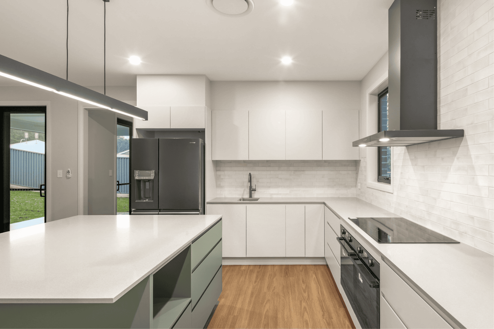 Modern white and green kitchen with island and stainless steel appliances.