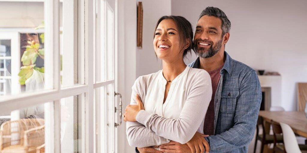 Bright happy couple admiring a new home through large house windows in a modern interior.