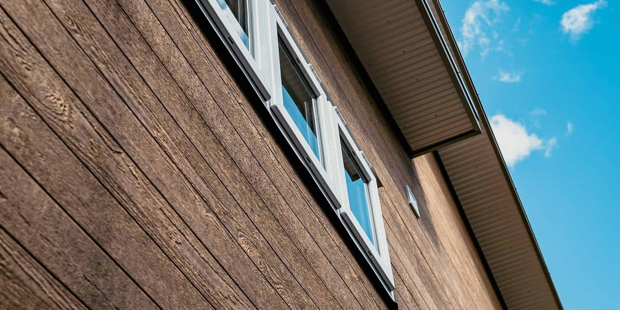 Modern wooden home exterior with white window shutters, under a blue sky with clouds.